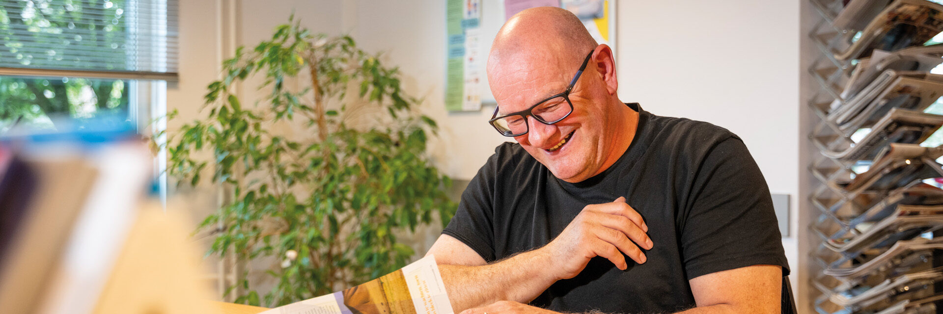 Man zit lachend in wachtkamer en leest een tijdschrift